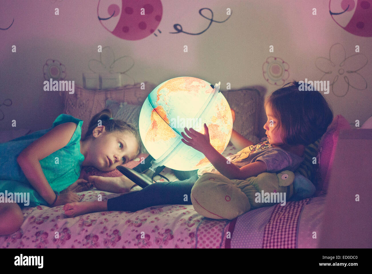 Zwei Mädchen (2-3, 6 und 7) Blick auf beleuchtete Lampe in Form eines Globus Stockfoto