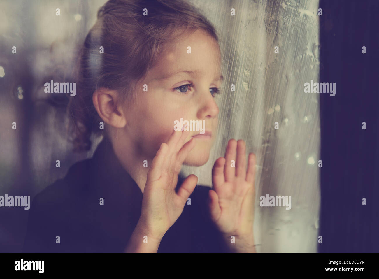 Trauriges Mädchen, das durch ein Fenster schaut Stockfoto