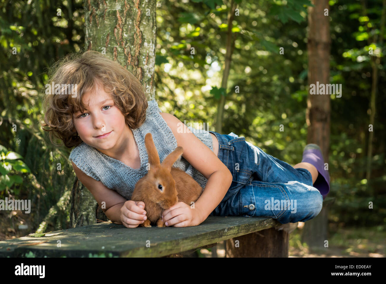 Junge (6-7) holding Hauskaninchen und liegend auf Bank im Wald Stockfoto
