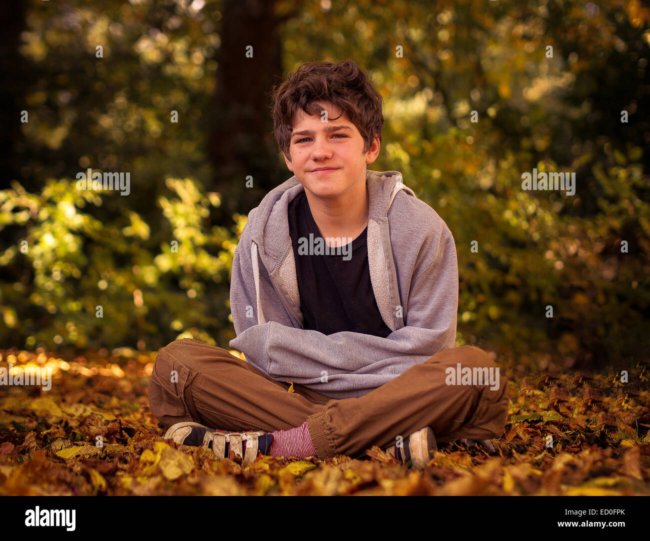 Junge sitzt mit gekreuzten Beinen im Herbstlaub Stockfoto