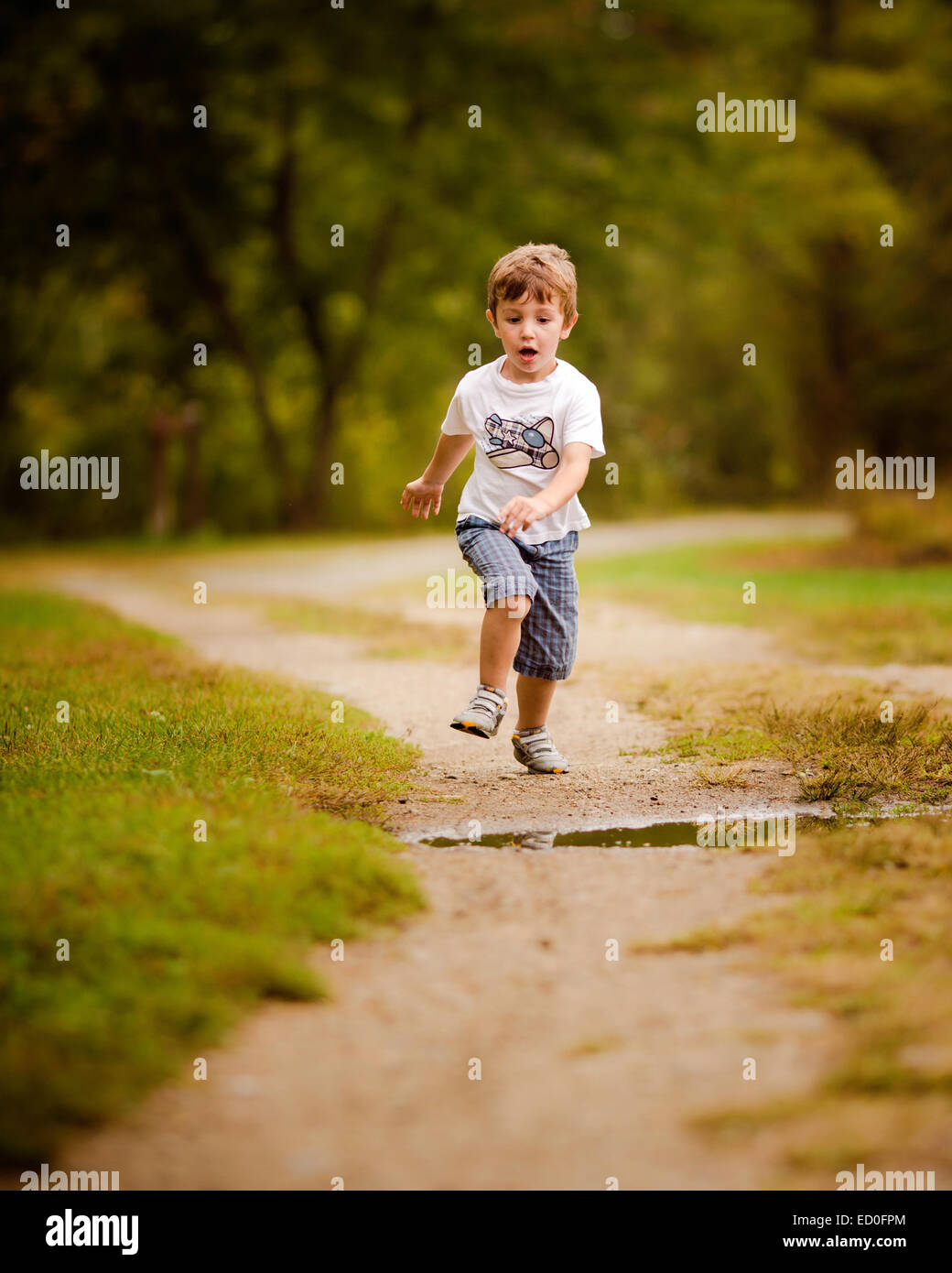 Junge läuft auf Fußweg etwa, über eine Pfütze zu springen Stockfoto