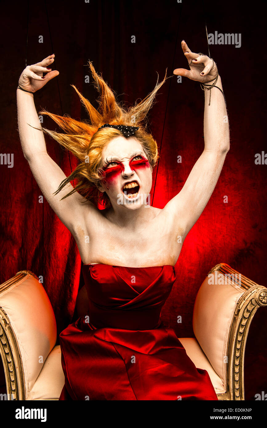 Fantasy-Verjüngungskur Fotografie - Seven Deadly Sins - Zorn: eine junge Frau-Mädchen-Modell mit stacheligen Punky Haar gebildet um zu schauen wie White-faced bemalte Puppe Porzellan und posiert wie eine Puppe in einem Fotostudio trägt eine rotes Kleid Kleid Ballkleid Stockfoto