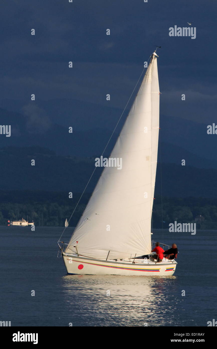 Weiße Segelboot segeln auf einen ruhigen Abend mit dramatischen Sonnenuntergang, Genfersee, Schweiz Stockfoto