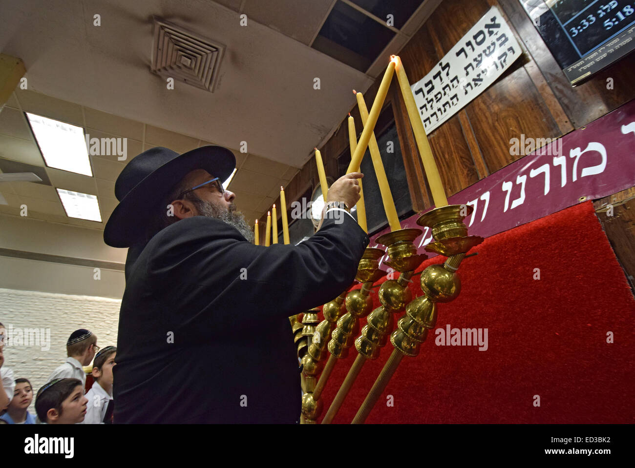 Eine orthodoxe jüdische Rabbiner zündet Hanukkah Kerzen als Student Gemeindemitglieder Watch auf eine Synagoge in Brooklyn, New York Stockfoto