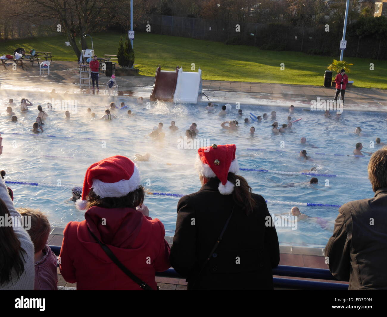London, UK. 25. Dezember 2014. Schwimmer nehmen an Hampton Freibad, Middlesex, an einem kalten klaren Weihnachtsmorgen. Warmen Poolwasser schafft einen Nebel.  Dieses Ereignis tritt jedes Weihnachten und ein freundlicher und fröhlichen Anlass für alle Altersgruppen ist. 2 Personen tragen Weihnachtsmann-Mützen. Bildnachweis: Charles Bowman/Alamy Live-Nachrichten Stockfoto