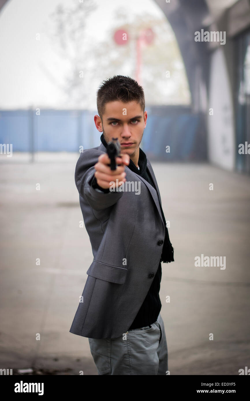 Gut gekleidet hübscher Junge Detektiv oder Polizisten oder Gangster stehen in einem städtischen Umfeld mit dem Ziel einer Feuerwaffe direkt an das Stockfoto