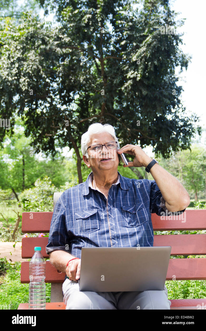 indische Greis Park Laptop und Telefon im Gespräch Stockfoto