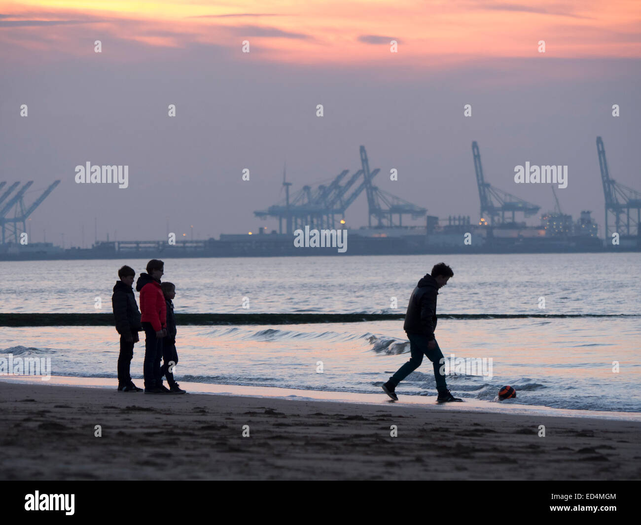 Eine Familie Fußball spielen am Strand bei Sonnenuntergang in Knokke-Heist, Belgien mit den Docks in Zeebrugge im Hintergrund Stockfoto