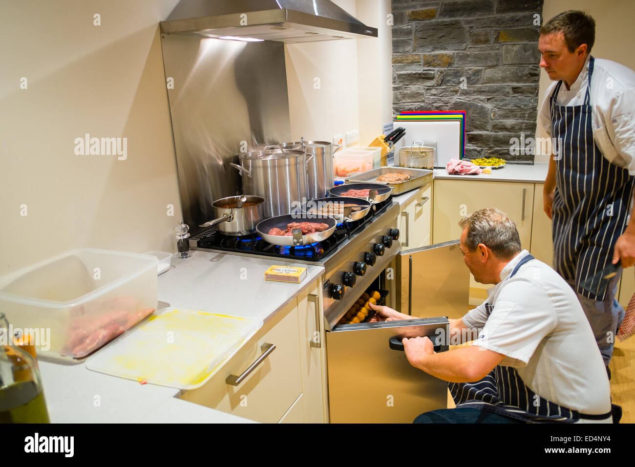 Zwei männliche Köche vorbereiten, Kochen einer Mahlzeit in einer modernen Küche, UK Stockfoto