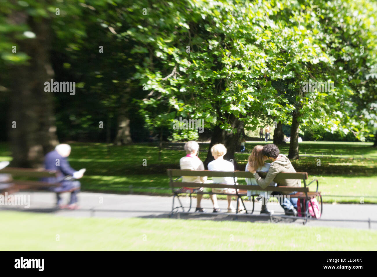 Menschen sitzen auf Bänken in einer Stadt; Ein junges Paar küssen und einige älteren Menschen. Stockfoto