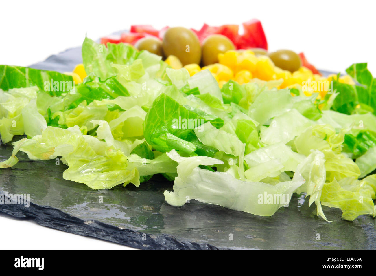 Nahaufnahme von einigen Salatzutaten, wie z. B. Kopfsalat, Mais, Oliven und Tomaten auf einem Schieferoberfläche Stockfoto