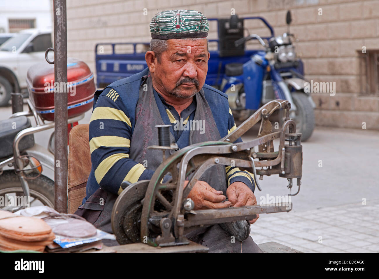 Schuhmacher / Schuh Handwerker bei der Arbeit auf der Straße in Qiemo / Cherchen, Oasenstadt in der Taklamakan-Wüste, Provinz Xinjiang, China Stockfoto