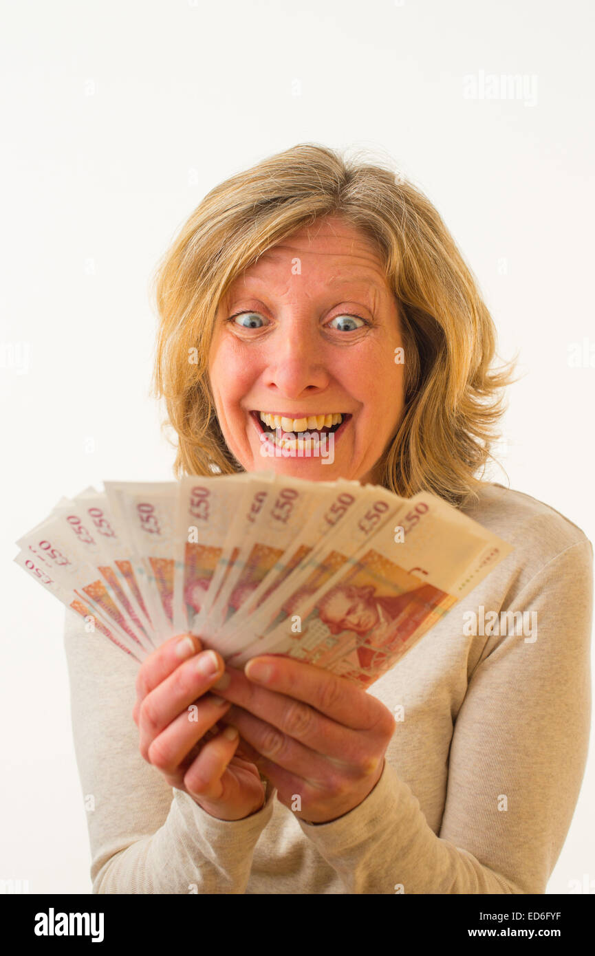 Eine vierzig Jahre alten kaukasischen Frau mit einer Handvoll von £50 Notizen Sterling Banknoten Bargeld suchen glücklich ekstatischen reichen, stehen vor einem weißen Hintergrund. UK Stockfoto