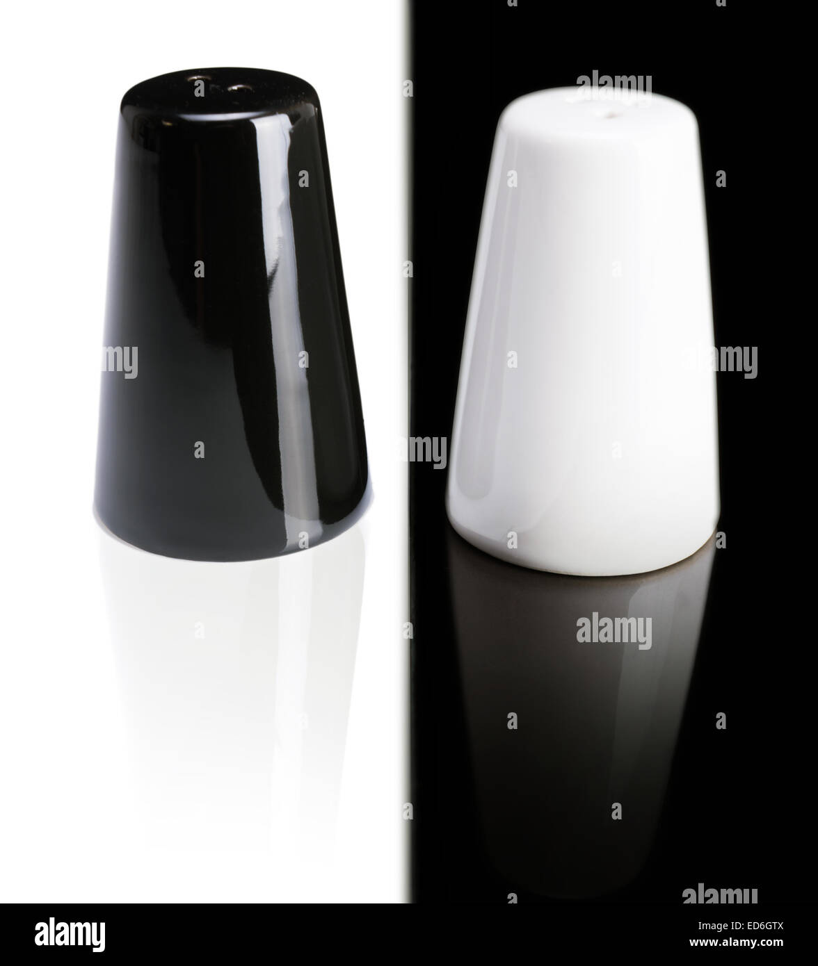 schwarzer Pfeffer Shaker auf einem weißen Hintergrund und einer weißen Salzstreuer auf schwarzem Hintergrund Stockfoto