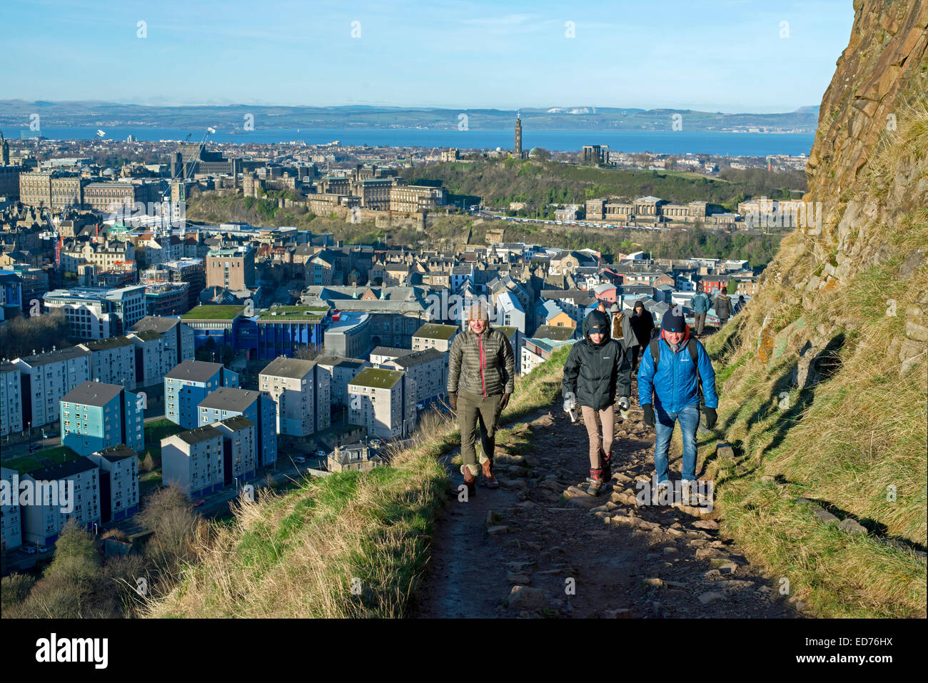 Wanderer auf dem Weg der radikalen unter Salisbury Crags mit der Altstadt von Edinburgh im Hintergrund an einem sonnigen Wintertag. Stockfoto