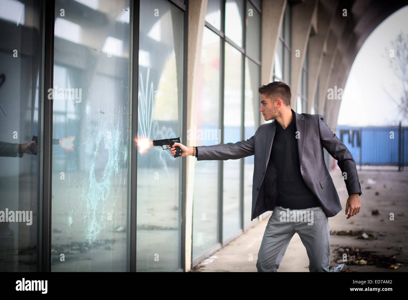 Jungen Detektiv oder Polizisten oder Gangster Abfeuern einer Pistole zu einem Fensterglas Stockfoto