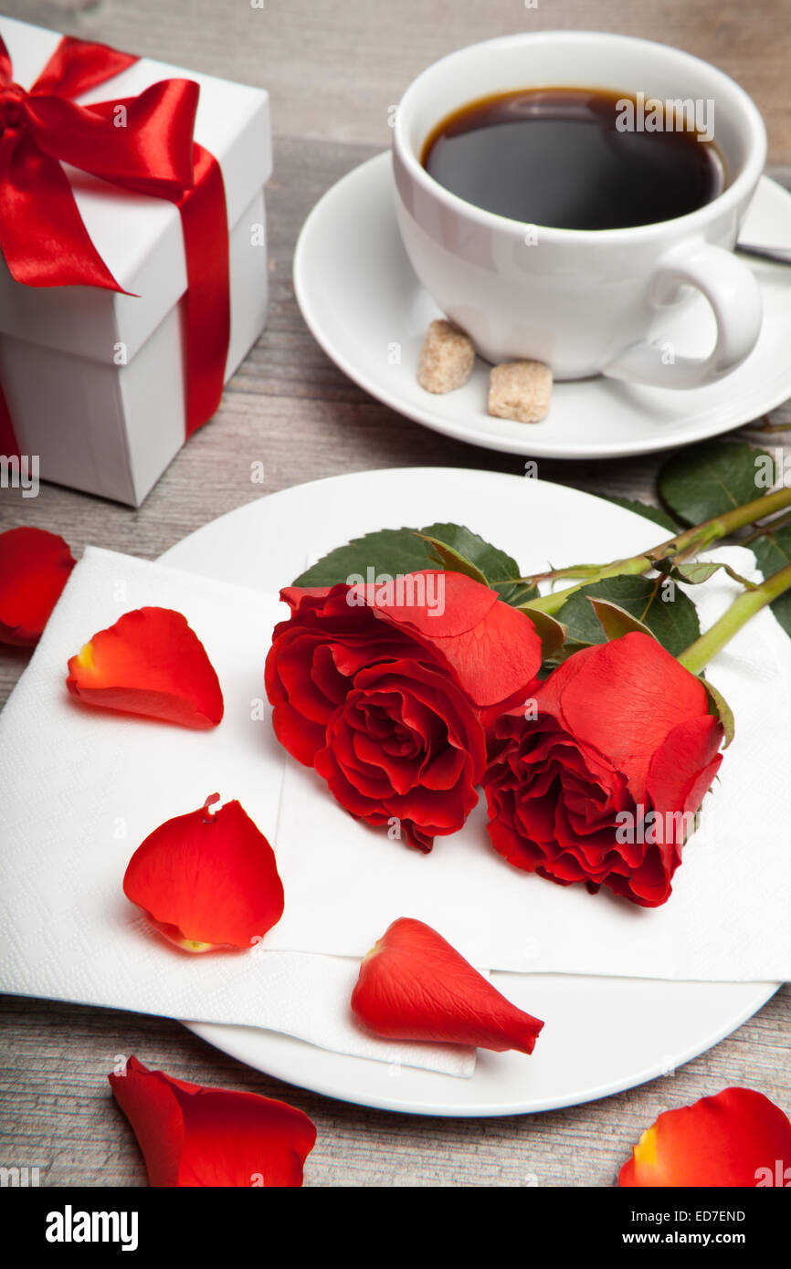 rote Rosen, Tasse Kaffee und Gegenwart auf einem Tisch Stockfoto