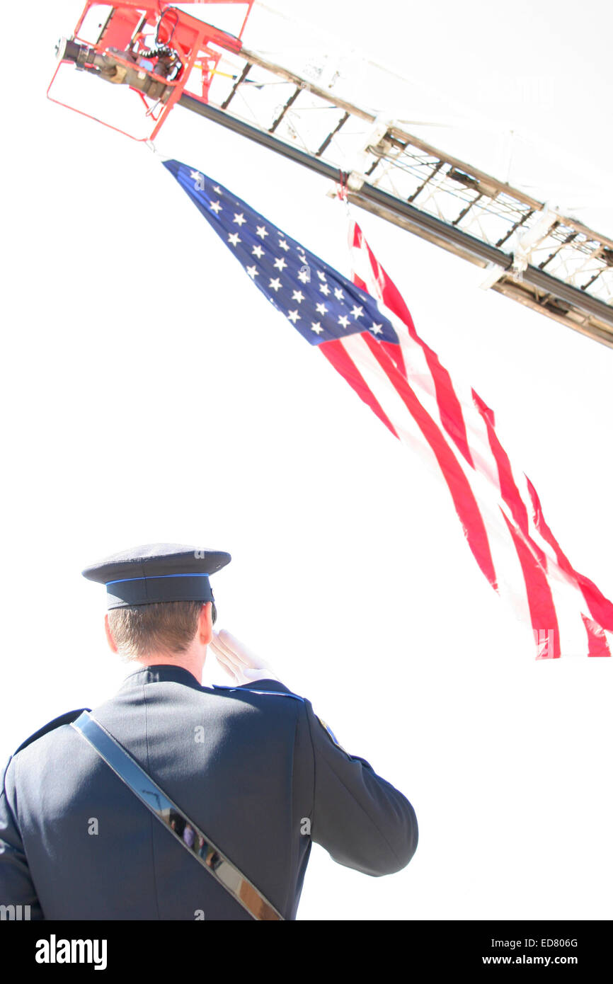 Ein Polizist begrüßte die amerikanische Flagge, die von einer Feuerwehr Leiter aufgehängt Stockfoto