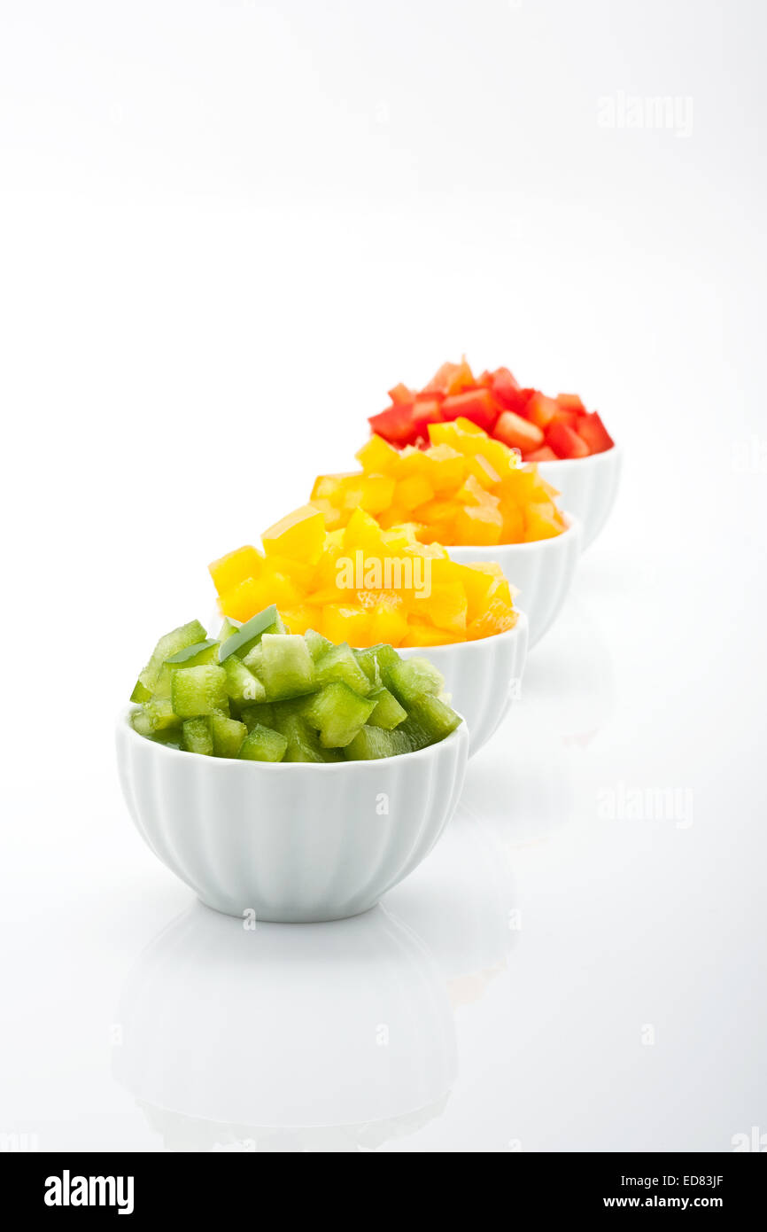 Nahaufnahme von frisch gehackte Stückchen grün gelbe und orange Paprika in Schalen isoliert auf weißem Hintergrund Stockfoto