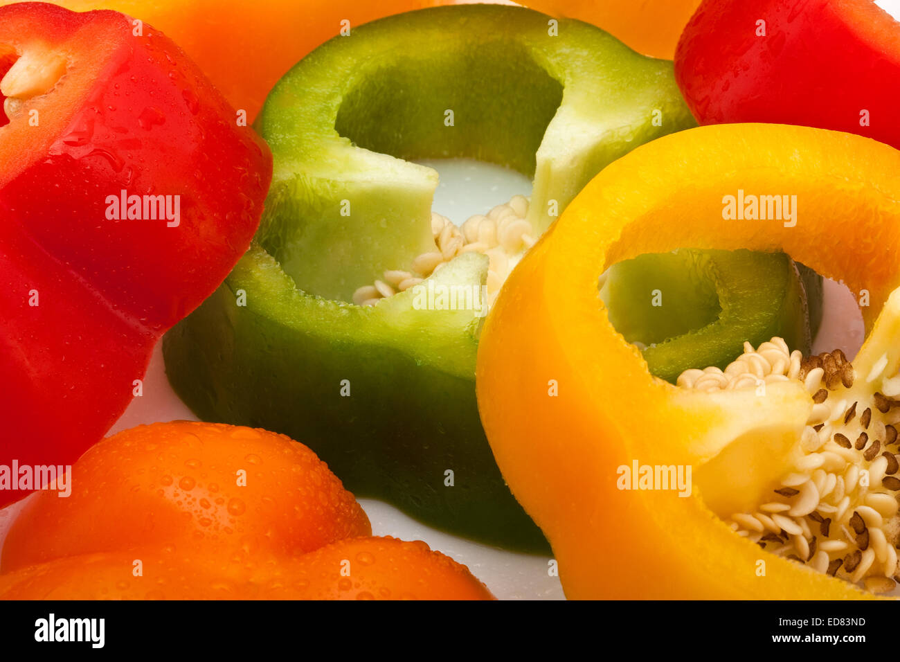 frisch geschnittene rote, grüne, gelbe und orange Paprika mit Wassertropfen isoliert auf weißem Hintergrund Stockfoto