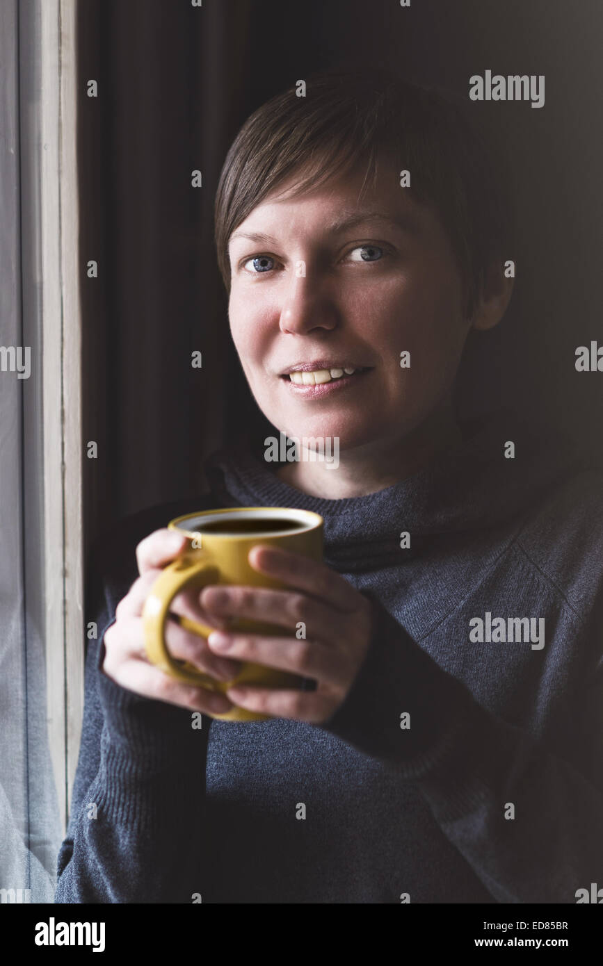 Schöne kaukasischen Erwachsenen lächelnde Frau trinken und genießen Kaffee im dunklen Raum. Selektiven Fokus mit geringe Schärfentiefe Stockfoto