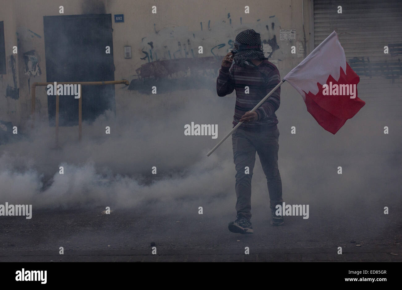 Ein Demonstrant trägt ein Bahrain Fahne inmitten Tränengas während einer Protestaktion wie bahrainische Sicherheitskräfte Demonstranten fordern Freiheit für Scheich Ali Salman unterdrücken, nachdem sie Scheich Ali Salman, Leiter der Al-Wefaq Gesellschaft - den größten Widerstand Gesellschaften in Bahrain - mehr als drei Tage lang festgehalten. © Hussain Albahrani/Pacific Press/Alamy Live-Nachrichten Stockfoto