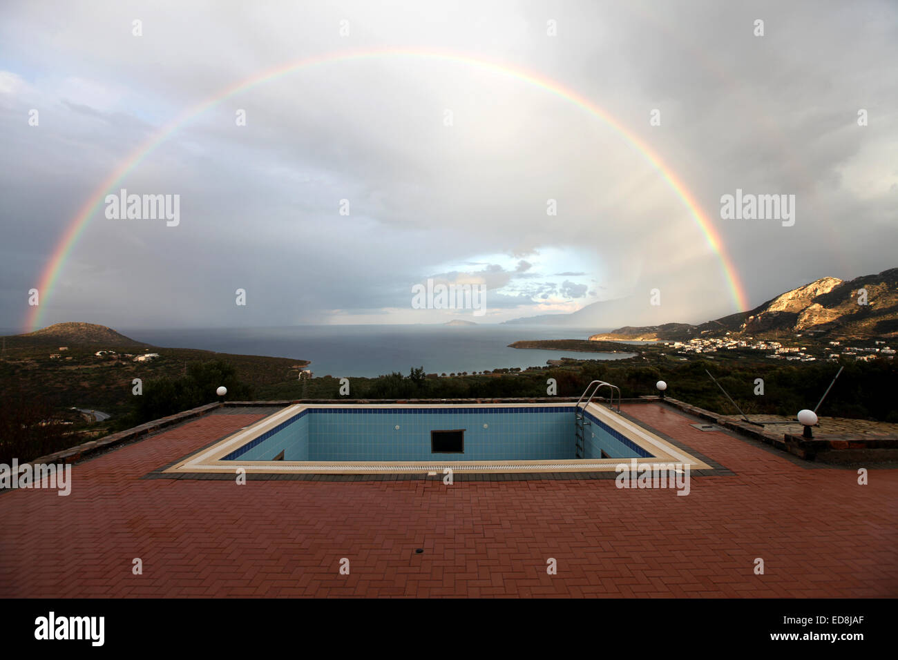 Ein Regenbogen über dem Schwimmbecken mit der Bucht von Mirabello, Crete als Kulisse Stockfoto