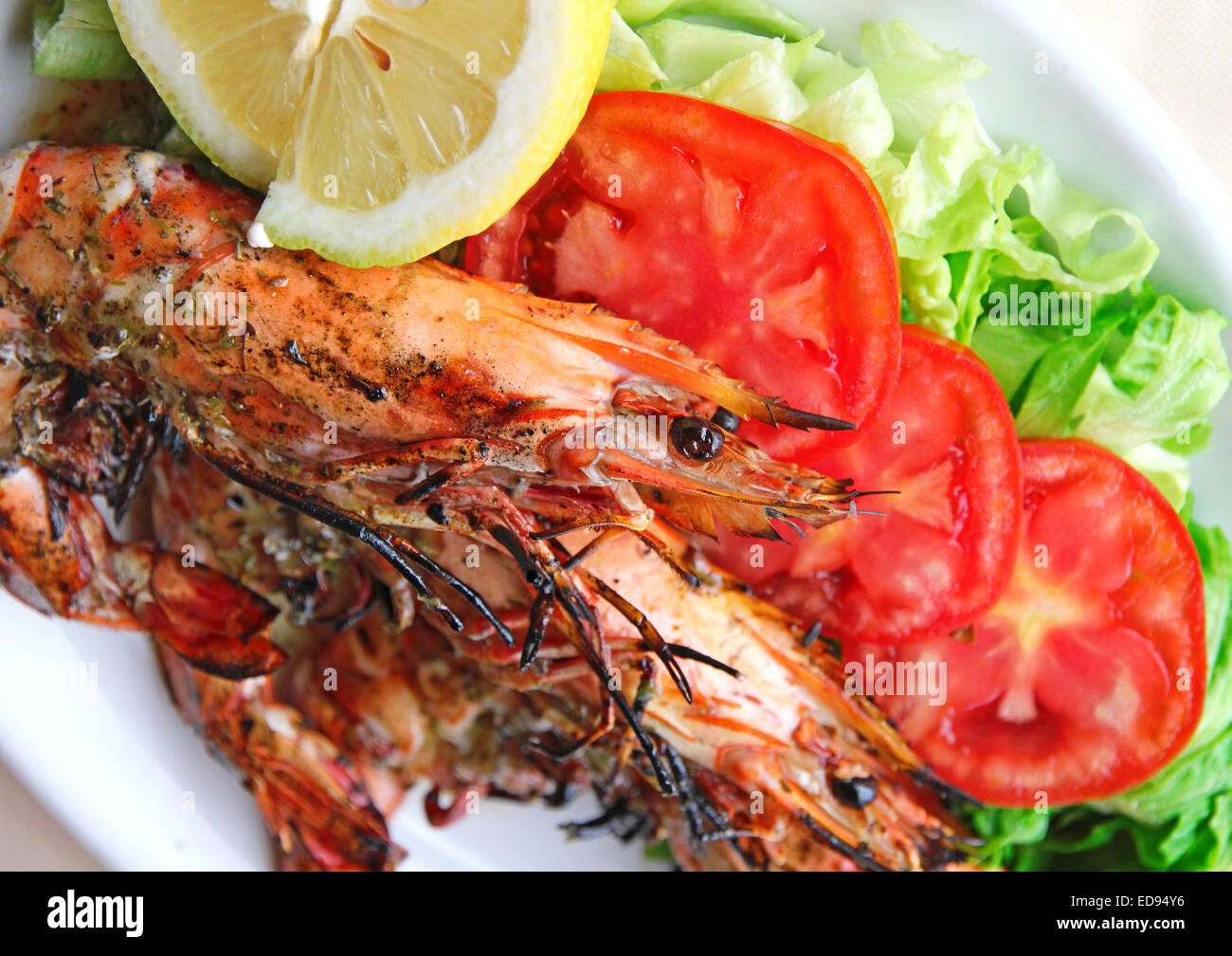 Frisch gegrillte Garnelen mit Tomaten, grünem Salat und Zitrone auf weißen Teller Stockfoto