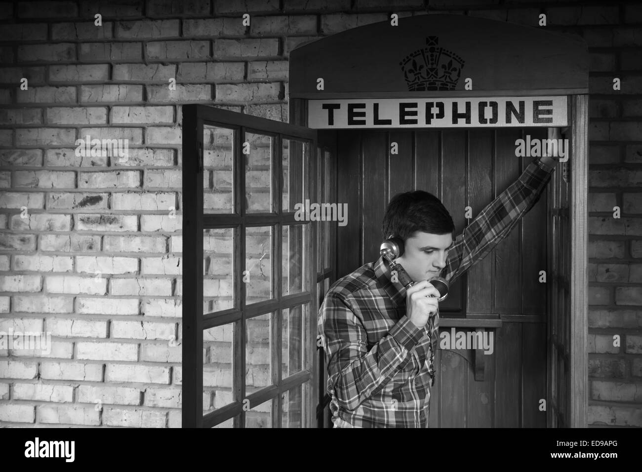 Junger Mann ruft jemand an die Telefonzelle mit Ziegel Wand Hintergrund. In Monochrom erfasst. Stockfoto