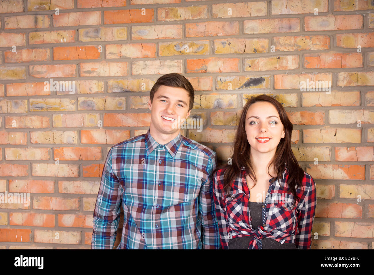 Taille, Porträt von lächelnd Young paar tragen Plaid Shirts stehen gemeinsam vor Backsteinmauer Stockfoto