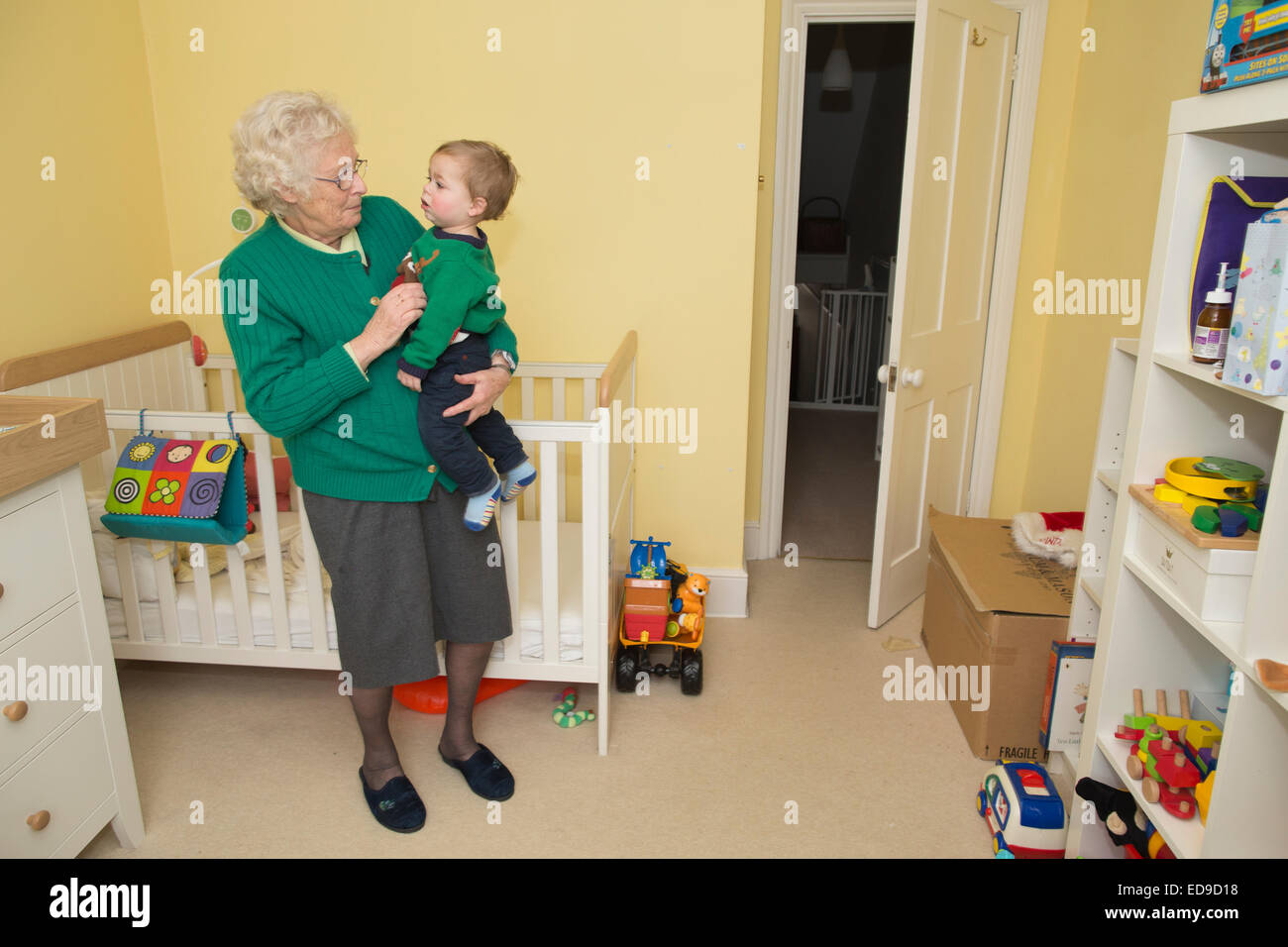 Ältere Großmutter mit ihrem (1 Jahr alt) Enkel in seinem Schlafzimmer Stockfoto