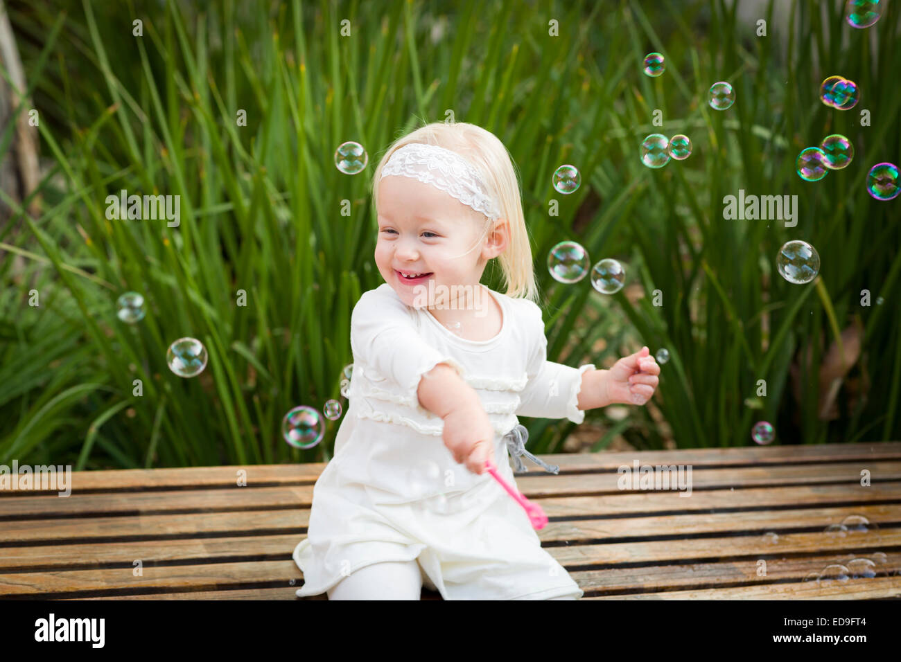 Entzückende kleine Mädchen auf Bank Spaß mit Bubbles draußen sitzen. Stockfoto