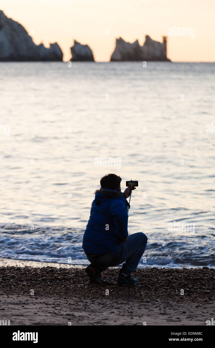 Ein Mann mit einem "Selfie Stick" in Alum Bay auf der Isle Of Wight mit den Nadeln in der Ferne Stockfoto