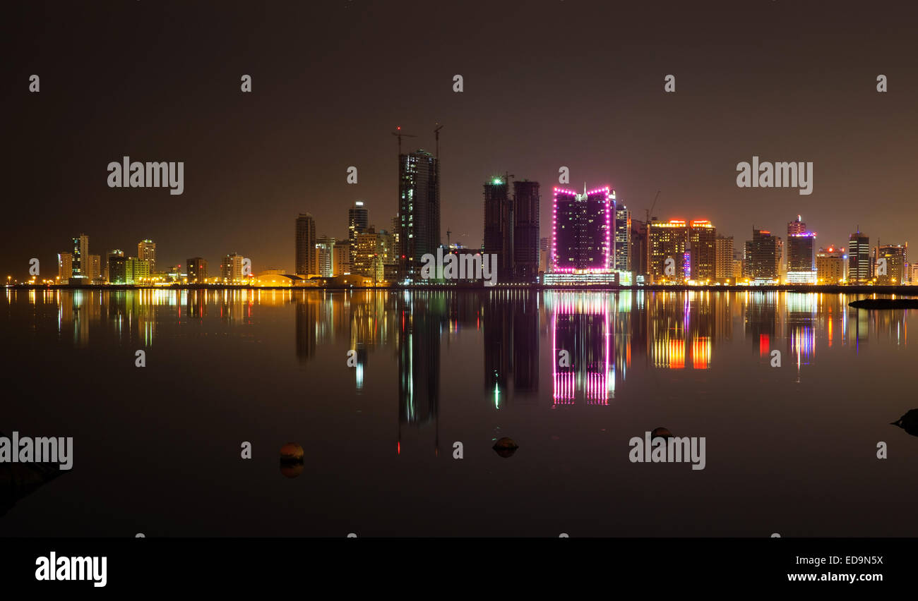 Nacht Skyline der modernen Stadt mit leuchtenden Neonröhren und Spiegelungen im Wasser. Manama, Bahrain, Naher Osten Stockfoto