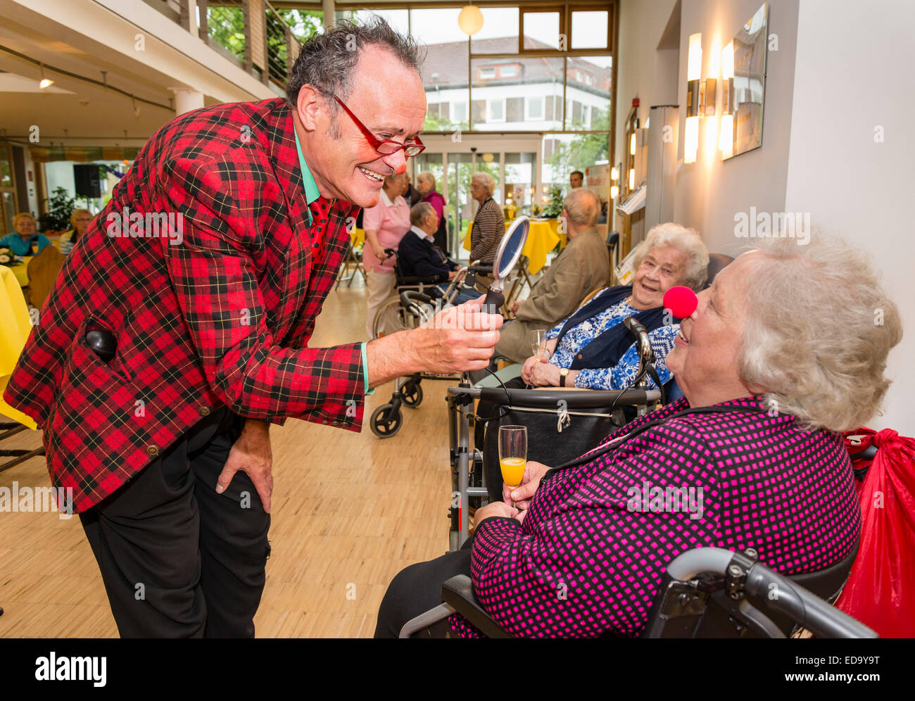 Ein Komiker, links, kam in einem Altersheim, Senioren mit seinen Witzen, mit einem Spiegel für eine ältere Dame zu gefallen Stockfoto