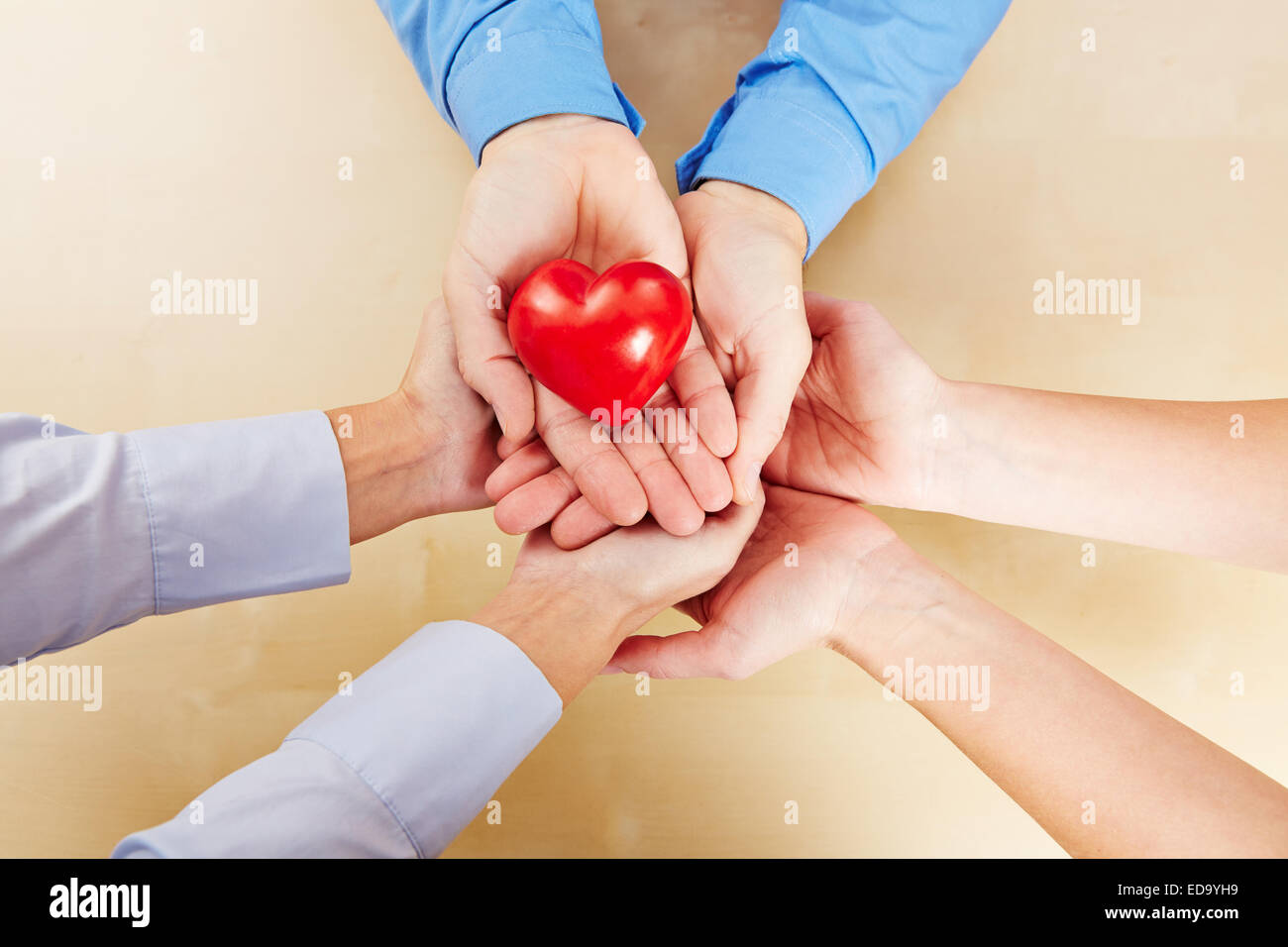 Viele Hände halten zusammen ein kleines rotes Herz Stockfoto
