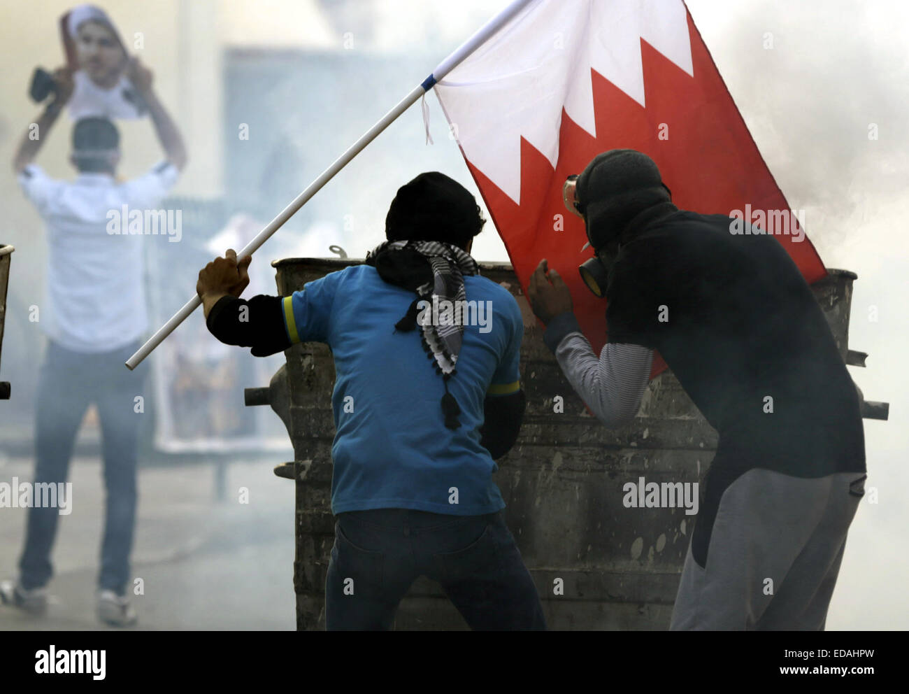 Manama, Bahrain. 3. Januar 2015. Eine bahrainische Anti-Regierungs-Demonstranten hält eine bahrainische Nationalflagge bei einem Zusammenstoß mit Anti-Aufruhr-Polizisten in Bilad Al Qadeem, in der Nähe von Manama, Hauptstadt von Bahrain, 3. Januar 2015. Zusammenstoß ist ausgebrochen, in vielen Teilen von Bahrain zwischen Anti-Polizei und Demonstranten, die die Freilassung des Landes größte schiitische Oppositionsführer Scheich Ali Salman fordern. © Hasan Jamali/Xinhua/Alamy Live-Nachrichten Stockfoto