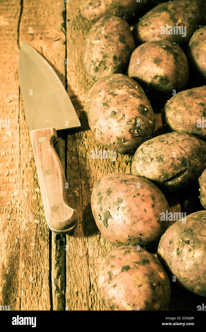 Echte frische Kartoffeln auf einem hölzernen Hintergrund und Messer Stockfoto