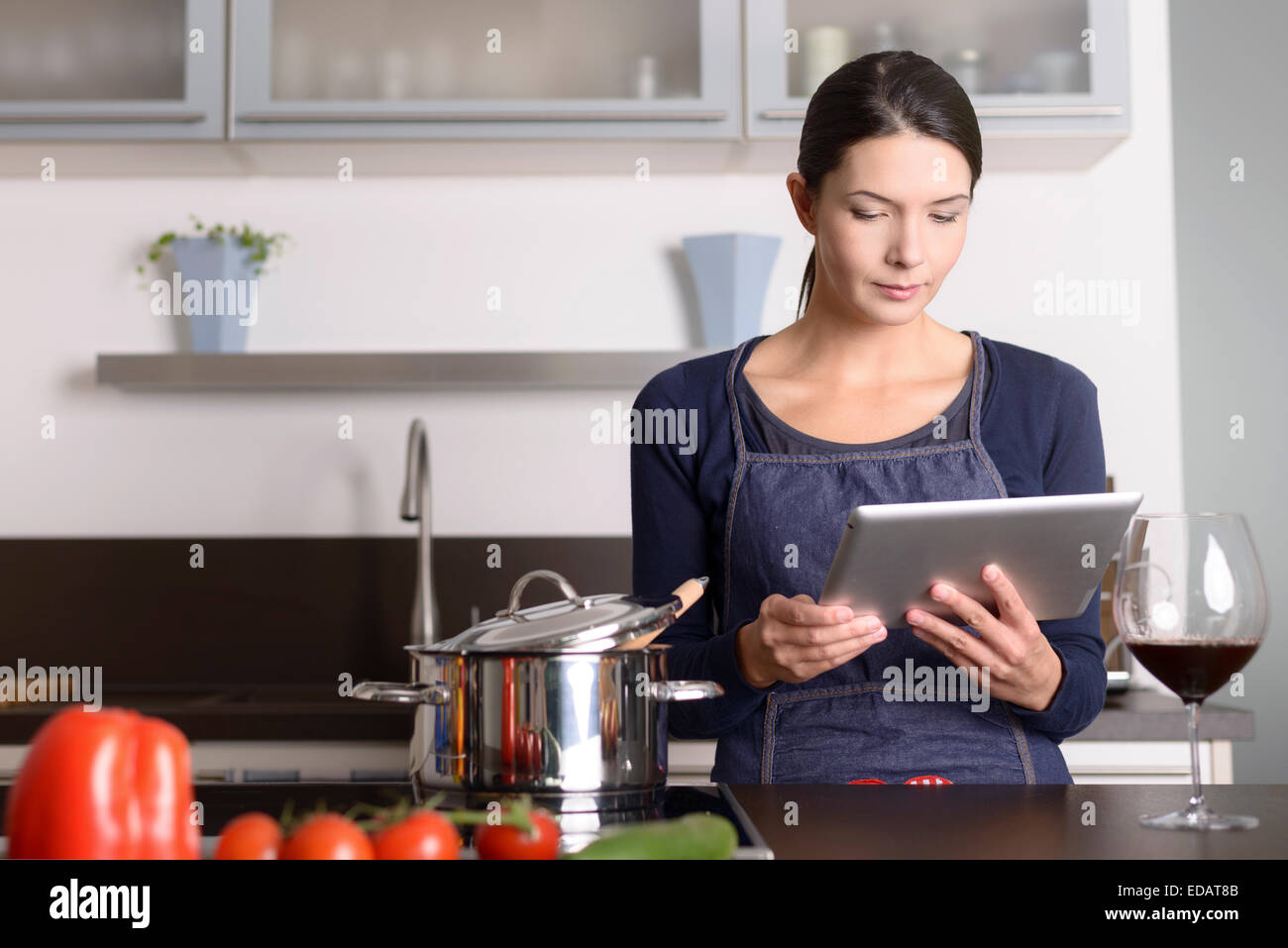 Junge Frau, die ein Rezept auf ihrem Tablet betrachten, während sie in der Küche vor einem Topf auf dem Herd steht Stockfoto