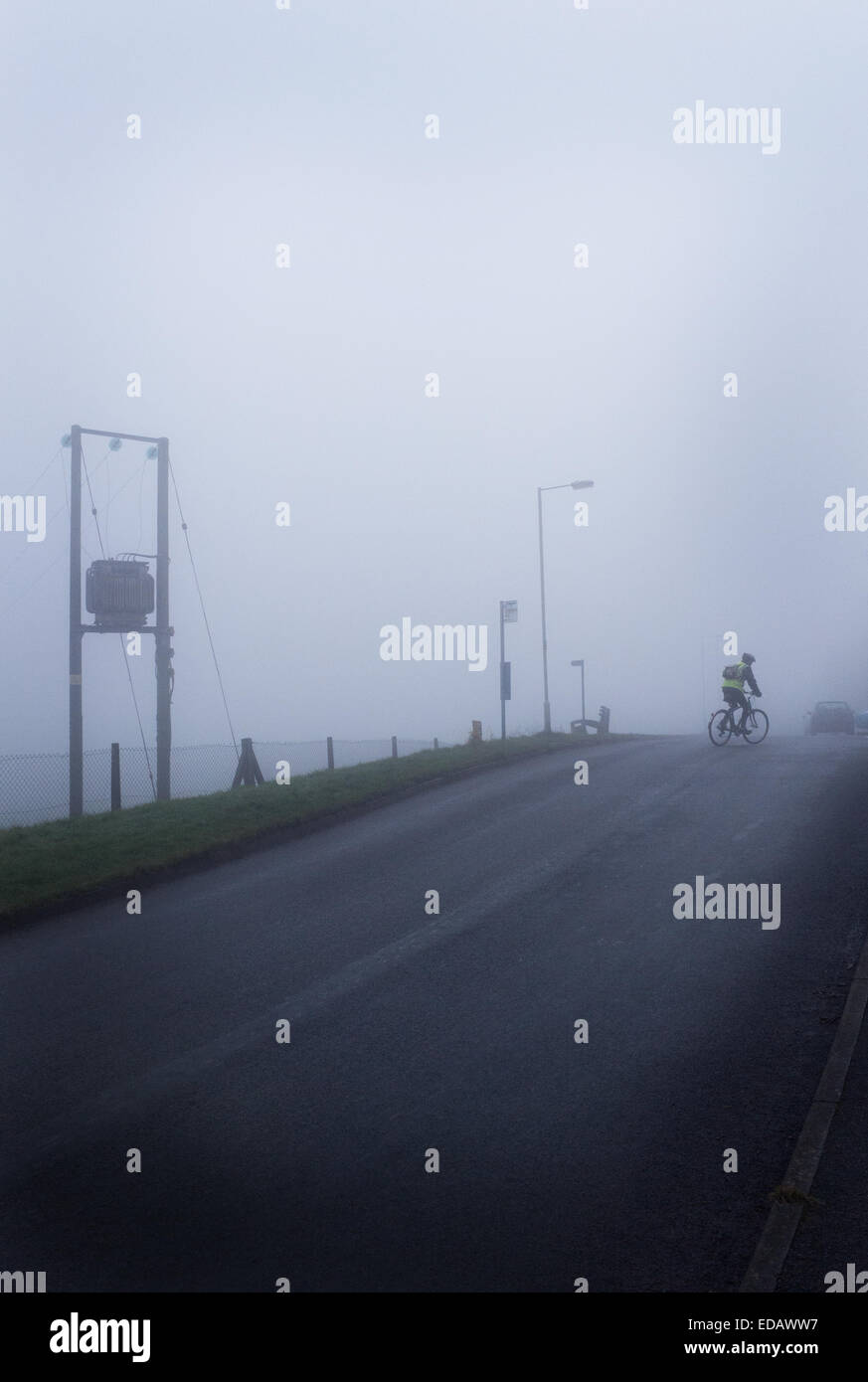 Nebel und Dunst auf einer abgelegenen Straße mit Radfahrer und Stromleitungen sichtbar. Stimmungsvolle Szene mit Platz für Art. Stockfoto
