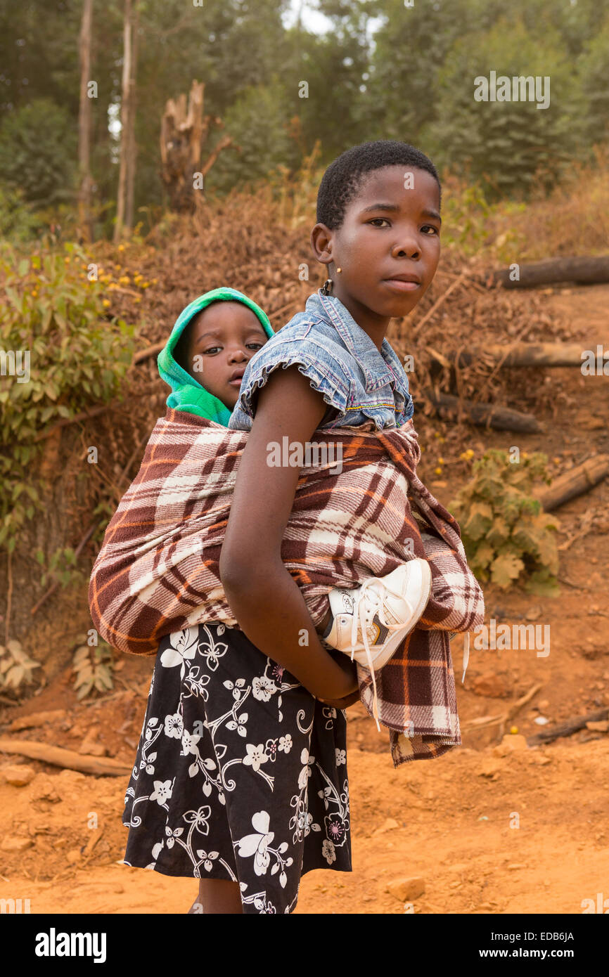 HHOHHO, Swasiland, Afrika - junges Mädchen trägt ihren Bruder auf dem Rücken, auf Feldweg. Stockfoto
