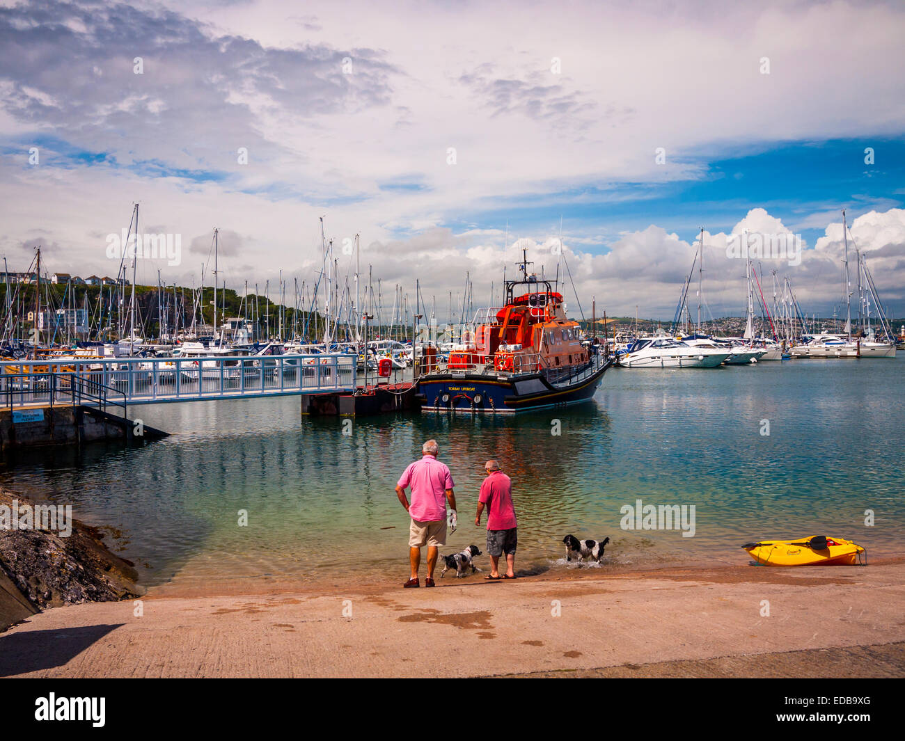 Zwei Männer zu Fuß ihre Hunde, bewundern Sie die Rnli lifeboat außerhalb Torbay Rettungsboot Station, Brixham, Großbritannien. Stockfoto