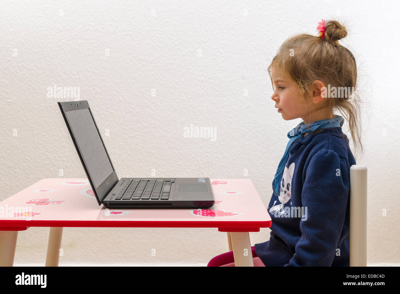 Mädchen, 3 Jahre, sitzt an einem Tisch vor einem laptop Stockfoto
