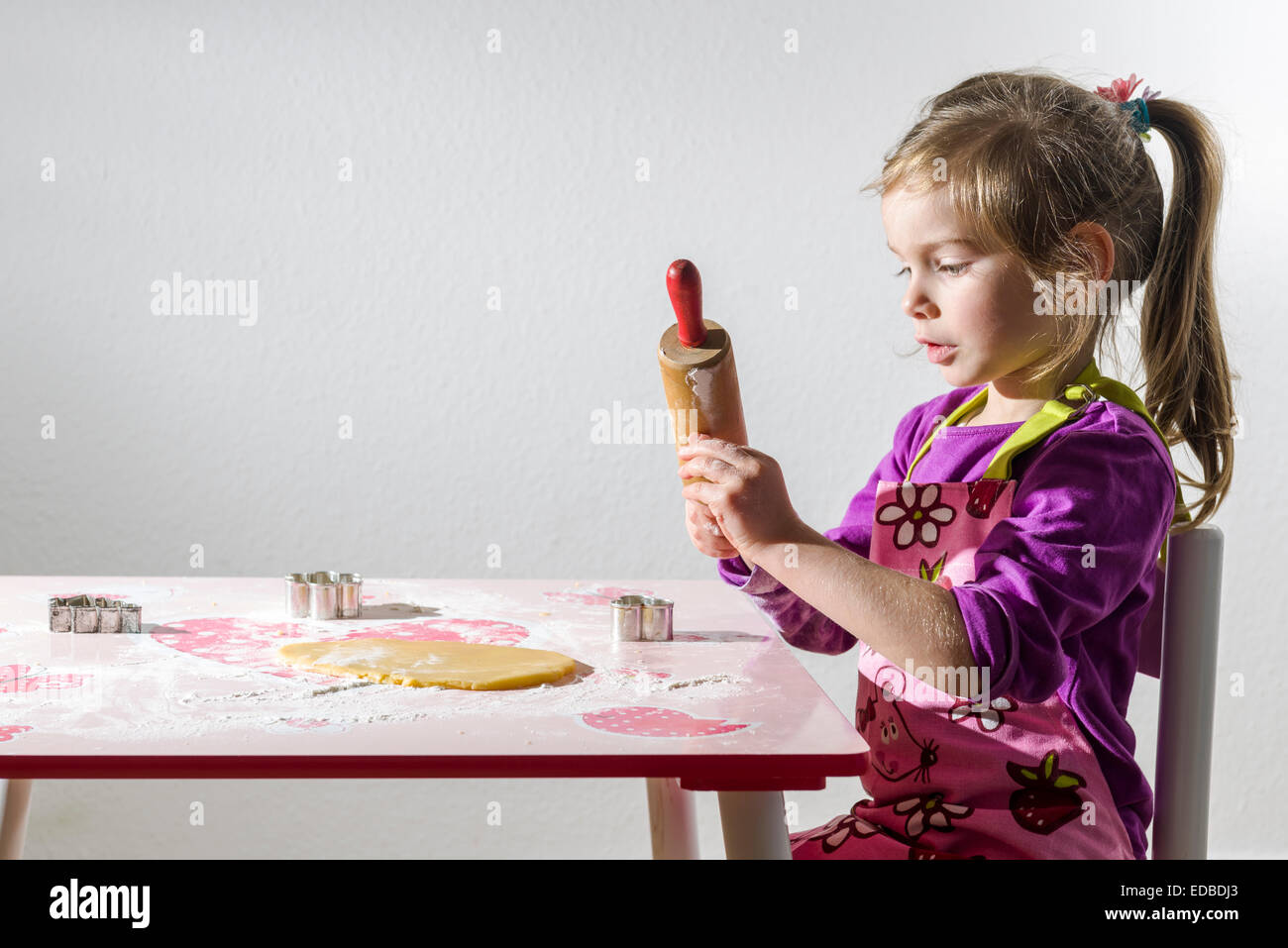 Mädchen, 3 Jahre, Weihnachtskekse backen, Teig ausrollen, auf einem Tisch Stockfoto