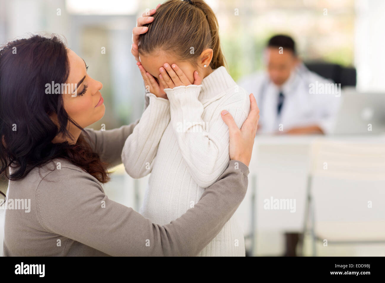 liebevolle Mutter tröstet ihre kranke Tochter in Arztpraxis Stockfoto