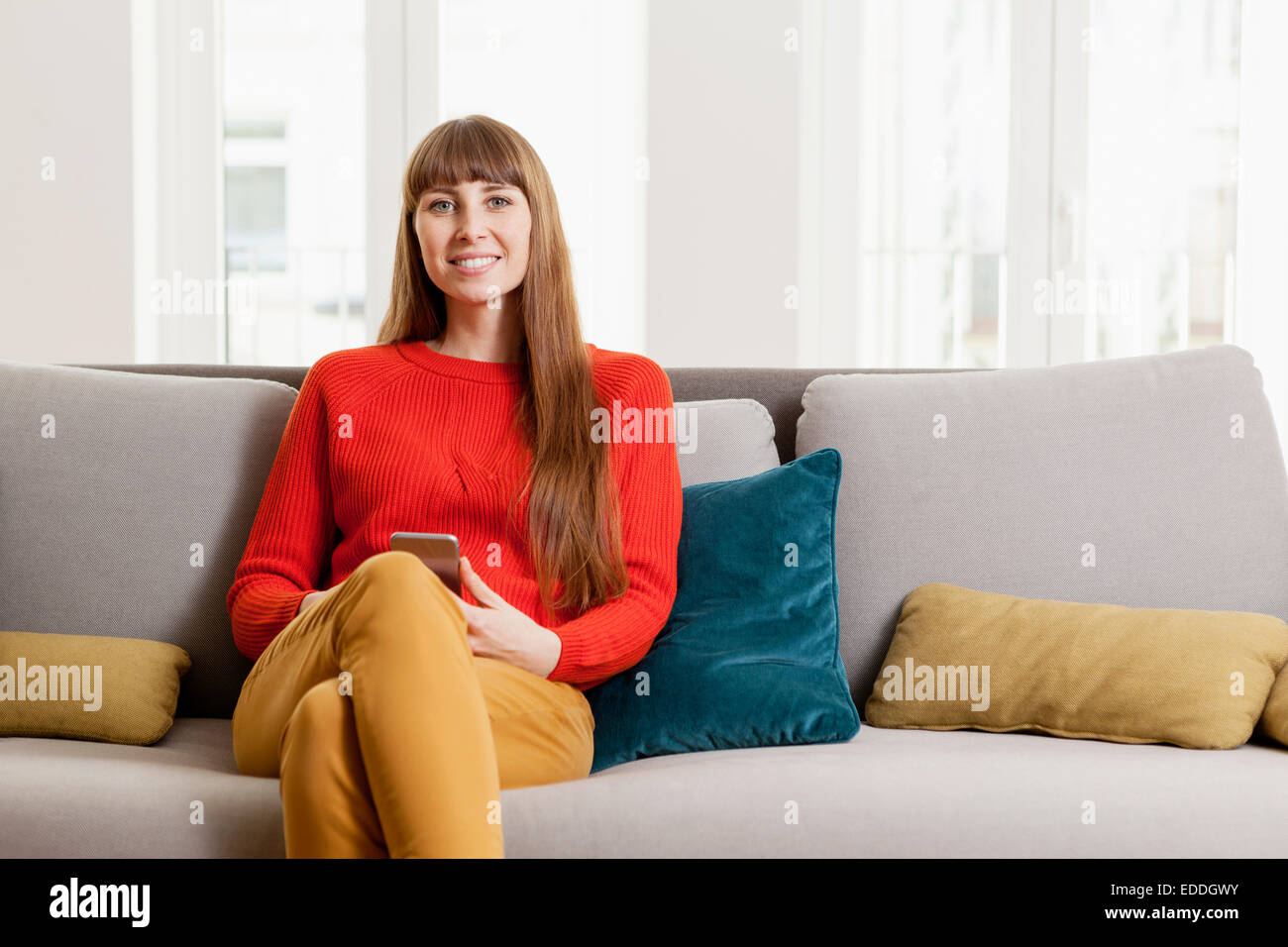 Lächelnde Frau sitzend auf Sofa mit Handy Stockfoto