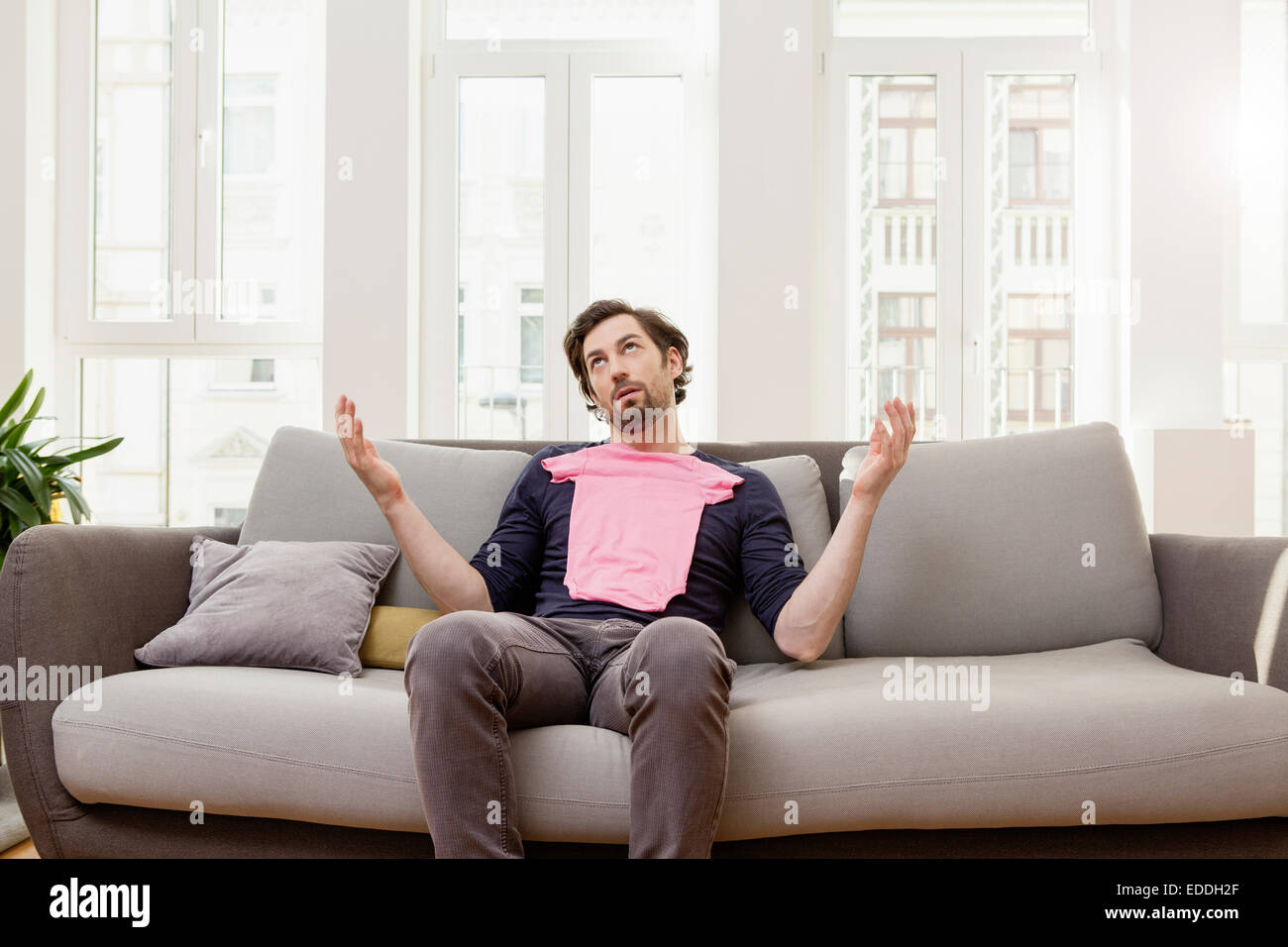 Enttäuschter Mann mit rosa Baby-Shirt auf couch Stockfoto