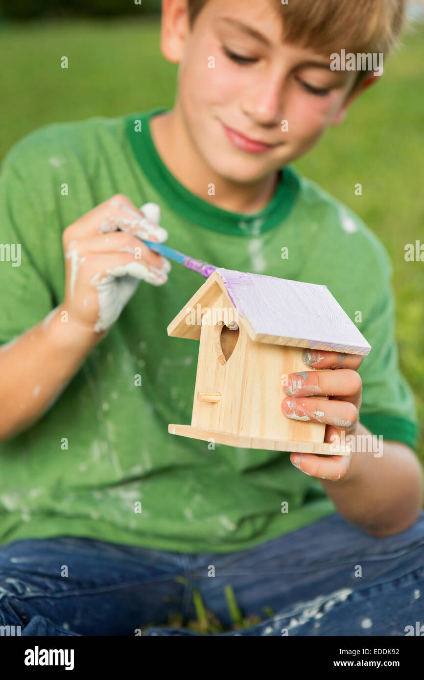 Ein Junge in einem Garten, malen ein Vogelhaus. Stockfoto