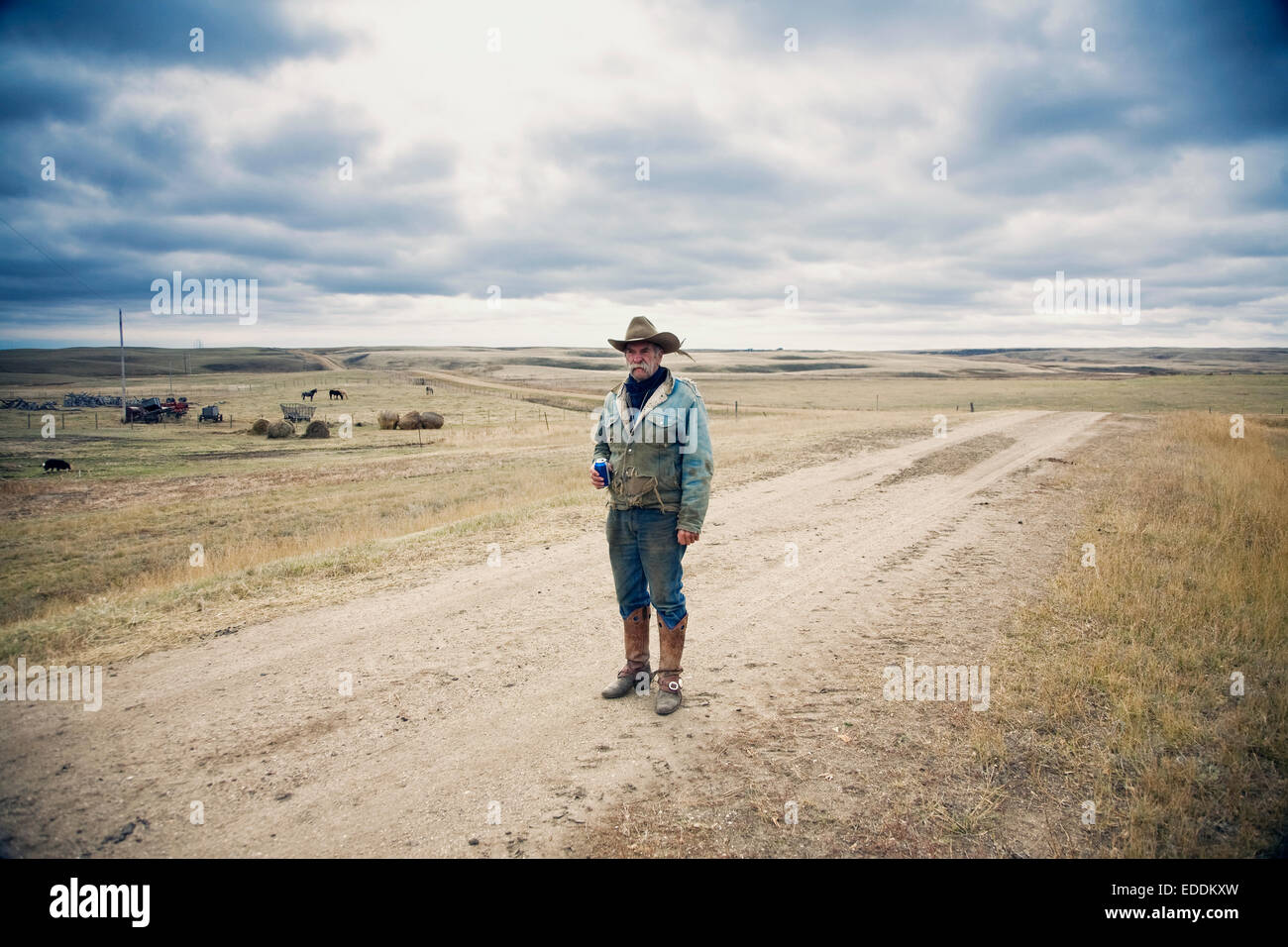 Mann mit Cowboyhut und Cowboy-Stiefel, stehend auf einem Feldweg in der kanadischen Prärie. Stockfoto