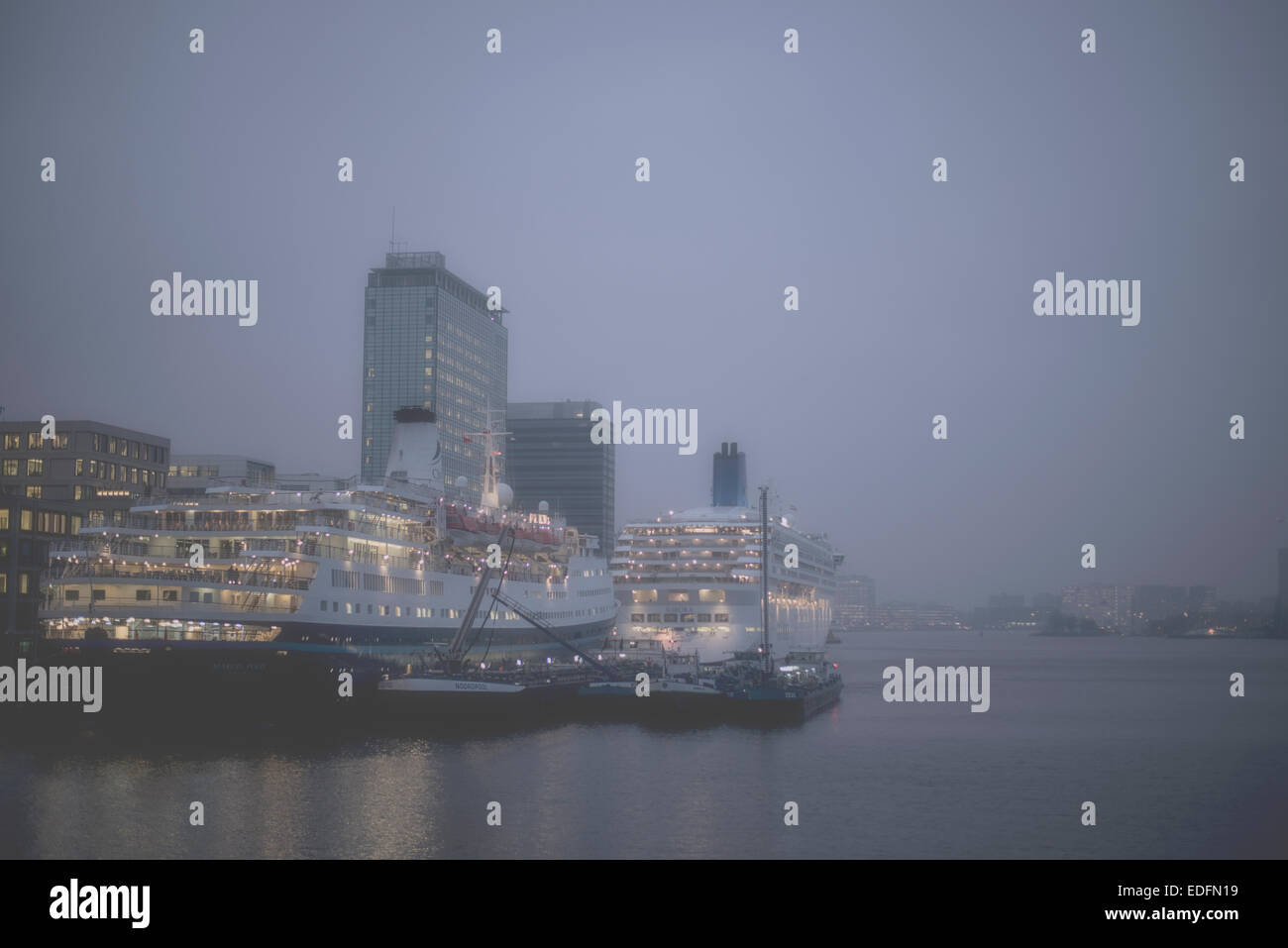 Zwei Kreuzfahrtschiffe vor Anker am Terminal Amsterdam Passagiere in der Abenddämmerung mit Skyline der Stadt im Hintergrund Stockfoto